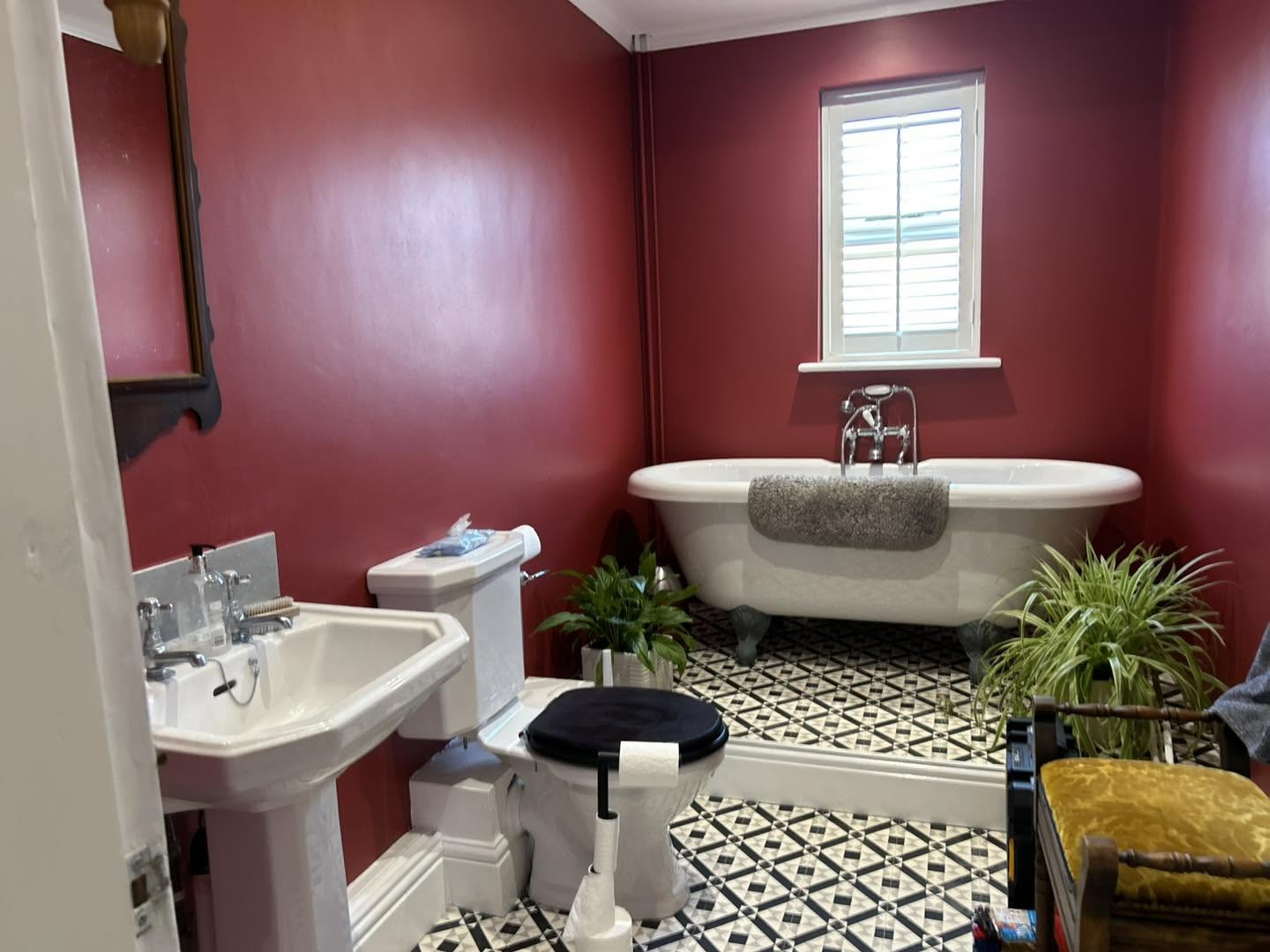 Deep crimson heritage bathroom with roll-top bath, panelled walls and monochrome tiled floor — decorated by S&J Interiors
