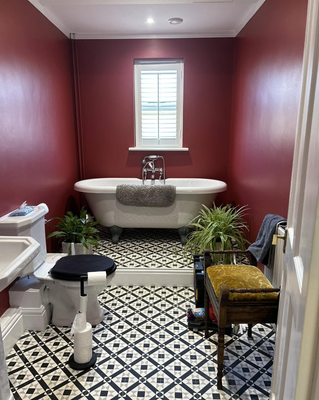 Deep red bathroom with roll-top bath and monochrome tiled floor